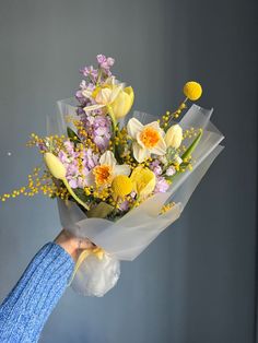 a person holding a bouquet of flowers in their hand with yellow and purple blooms on it