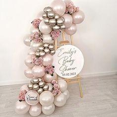 a baby shower sign surrounded by balloons and flowers on a wooden easer in front of a white wall