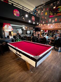 a red pool table in a room with people sitting around and tables on the floor