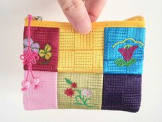 a hand holding a small purse made out of different colored squares and flowers on it