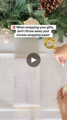 someone wrapping christmas presents on a table with paper and scissors in front of the tree