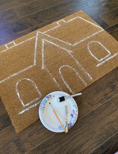 a brown door mat with a house drawn on it next to a plate and paintbrush