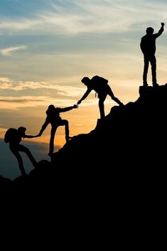 three people helping each other climb up a mountain at sunset or sunrise with their hands in the air