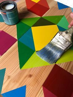 a person using a paintbrush on top of a wooden table covered in colorful geometric shapes