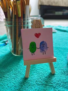 a small easel with some paint and pencils in it sitting on a blue rug