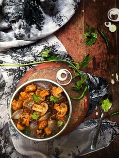 a bowl filled with shrimp and vegetables on top of a wooden table next to a cloth