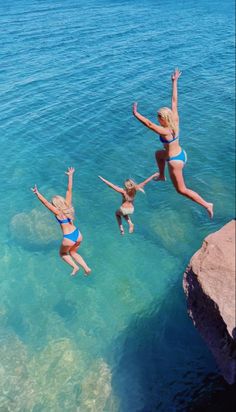 three women jumping into the water from rocks in front of their heads and arms, while another woman looks on