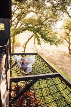 a man sitting in a hammock on the back deck of a house with trees