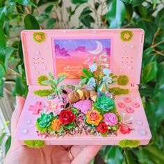 someone holding up a pink toy laptop with flowers and plants on it