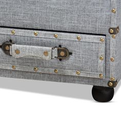 an upholstered grey linen chest with brass rivets on the front and sides