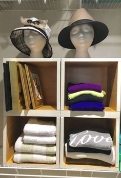 hats and towels are displayed on shelves in a store display case, with two mannequins behind them