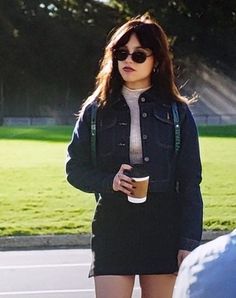 a woman in black jacket and skirt holding a coffee cup while standing next to a car