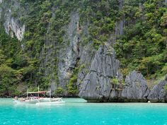 a boat is in the water near some rocks and trees on the side of a mountain