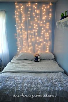 a bed with white sheets and lights on the headboard, in front of a window