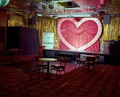 an empty stage set up with chairs and tables in front of a heart - shaped curtain