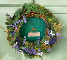 a wreath is hanging on the front door with flowers and greenery around it's edges