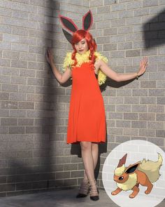 a woman in an orange dress is standing next to a brick wall with her hands out