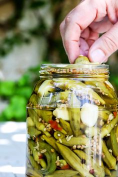 a jar filled with pickles sitting on top of a table next to a person's hand