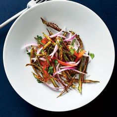 a white bowl filled with vegetables on top of a blue table cloth next to chopsticks