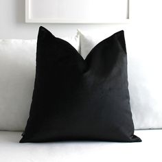 a black pillow sitting on top of a white couch next to a framed picture above it