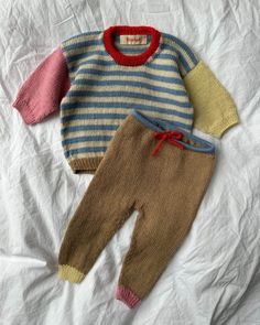 two baby sweaters laying on top of a bed next to an adult sized doll