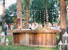 an outdoor bar is set up for a wedding reception with lanterns and flowers hanging from the trees