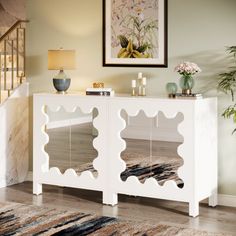 a white sideboard with mirrors on it in front of a stair case and potted plant