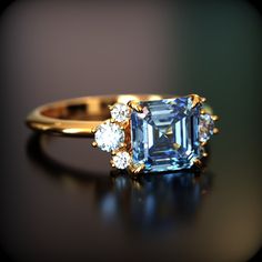 an emerald and diamond ring sitting on top of a black surface with three diamonds around it