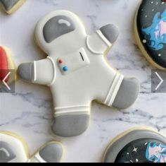 cookies decorated to look like astronauts are laying on a marble counter top with space themed cookies in the background