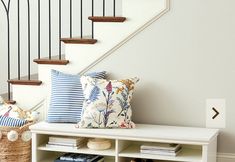 a white bench with pillows on it next to a stair case and bookshelf