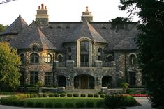 a large stone house surrounded by lush green trees and bushes in the foreground is a circular driveway