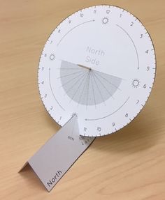 a paper clock with a ruler on it sitting on top of a wooden table next to a tag