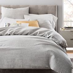 a bed with grey linens and pillows in a bedroom area next to a window