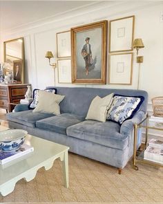 a living room with blue couches and pictures on the wall above them in gold frames