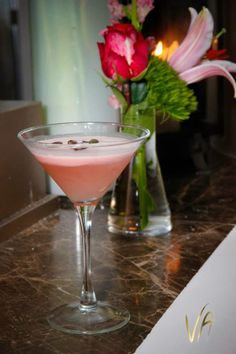 a pink drink sitting on top of a table next to a vase with flowers