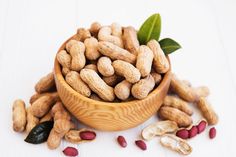 peanuts in a wooden bowl with leaves on the top and other nuts scattered around it