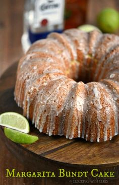 a bundt cake with icing and limes on a cutting board next to a bottle of margarita