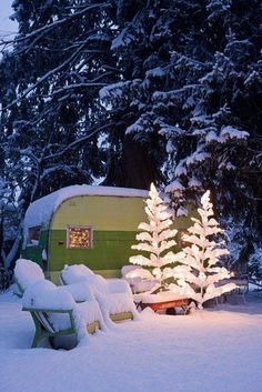 a green and white trailer sitting in the snow next to a tree with lights on it