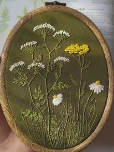 someone is holding up a small embroidery project with flowers on the front and side of it