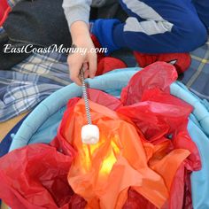 a young boy is playing with an orange light in a blue basket filled with plastic bags