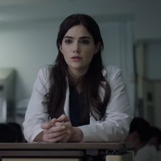 a woman sitting at a table with her hands folded in front of her chest and looking off to the side