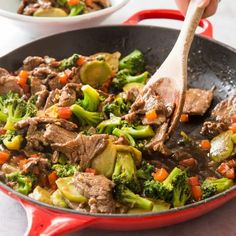 a skillet with beef, broccoli and carrots being stirred by a wooden spoon