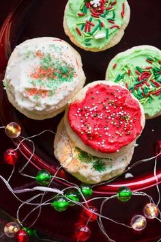 three decorated cookies sitting on top of a black plate next to christmas lights and decorations