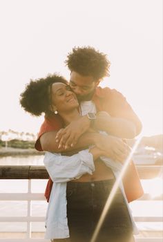 a man and woman embracing each other on a bridge near the water with sun shining through them