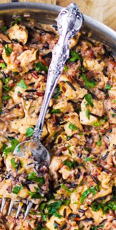 a pan filled with chicken and vegetables on top of a wooden table next to a fork