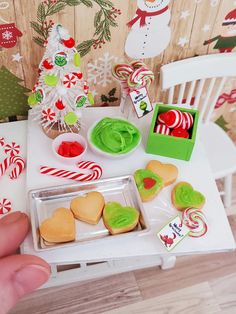 a person is holding a tray with cookies and candy in front of a christmas tree