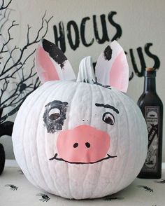 a white pumpkin decorated to look like a pig with black ears and nose painted on it