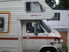 an old camper is parked in front of a white building with red, yellow and orange stripes