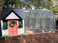 a chicken coop with a red door and window on the side, surrounded by mulch