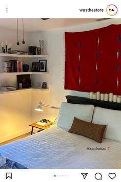 a bed room with a neatly made bed and a red wall hanging over it's headboard